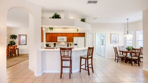 A spacious kitchen with a central island, wooden cabinets, and a dining area with a table and chairs. - Gorgeous home near Disney with private pool, pool spa, on-site gym, tennis, AC (Davenport)