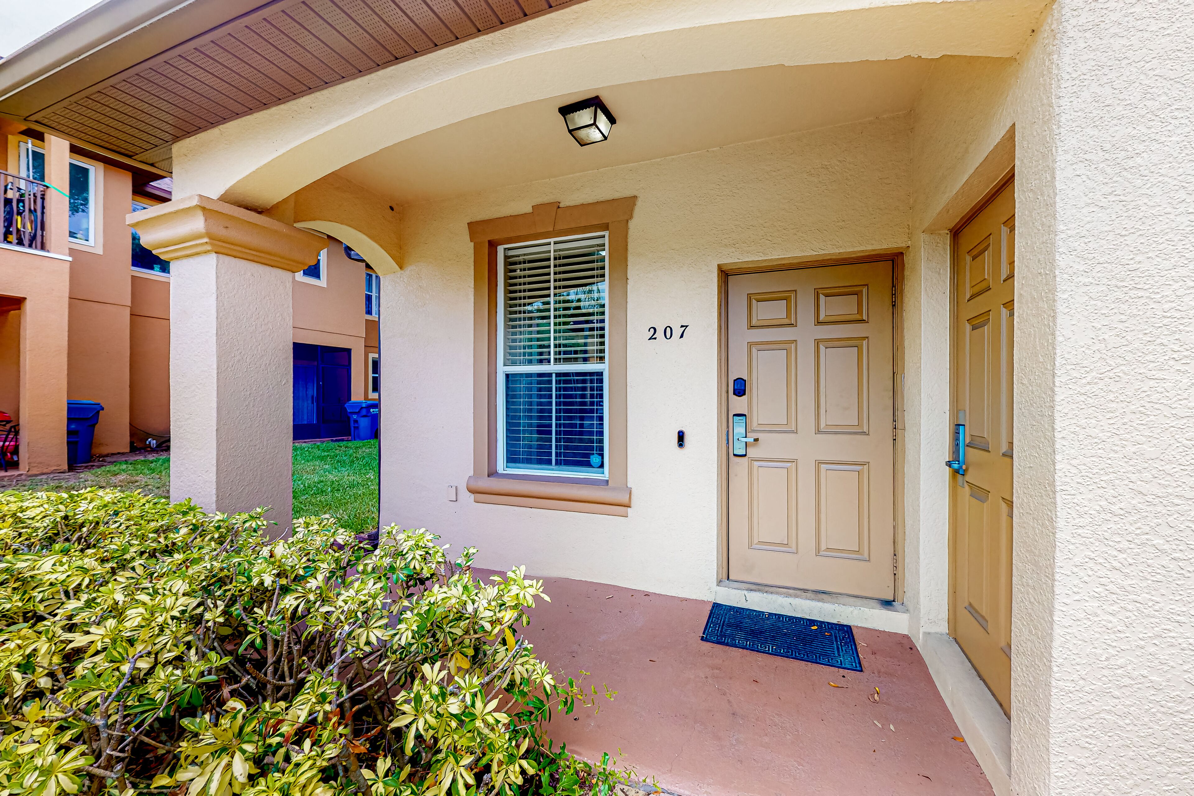 A building entrance with a beige door, a window with blinds, and a number 207 on the wall.