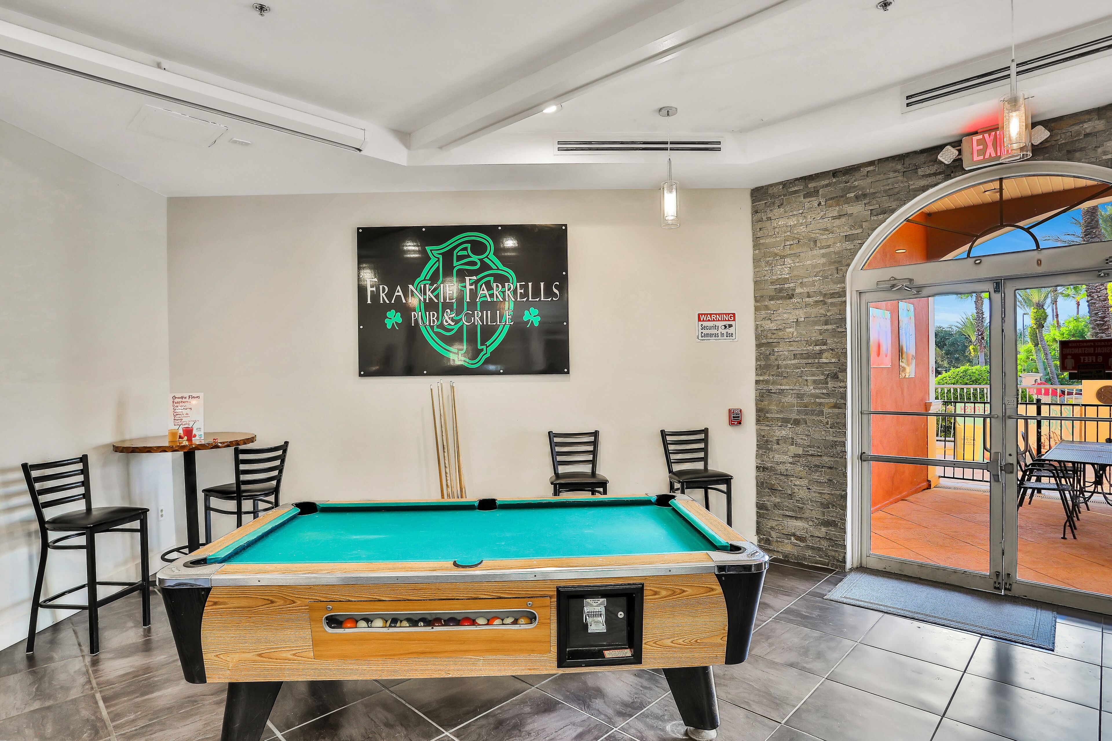 A pool table with chairs, a sign for Frankie Farrells Pub & Grill, and a view of the outdoor patio.