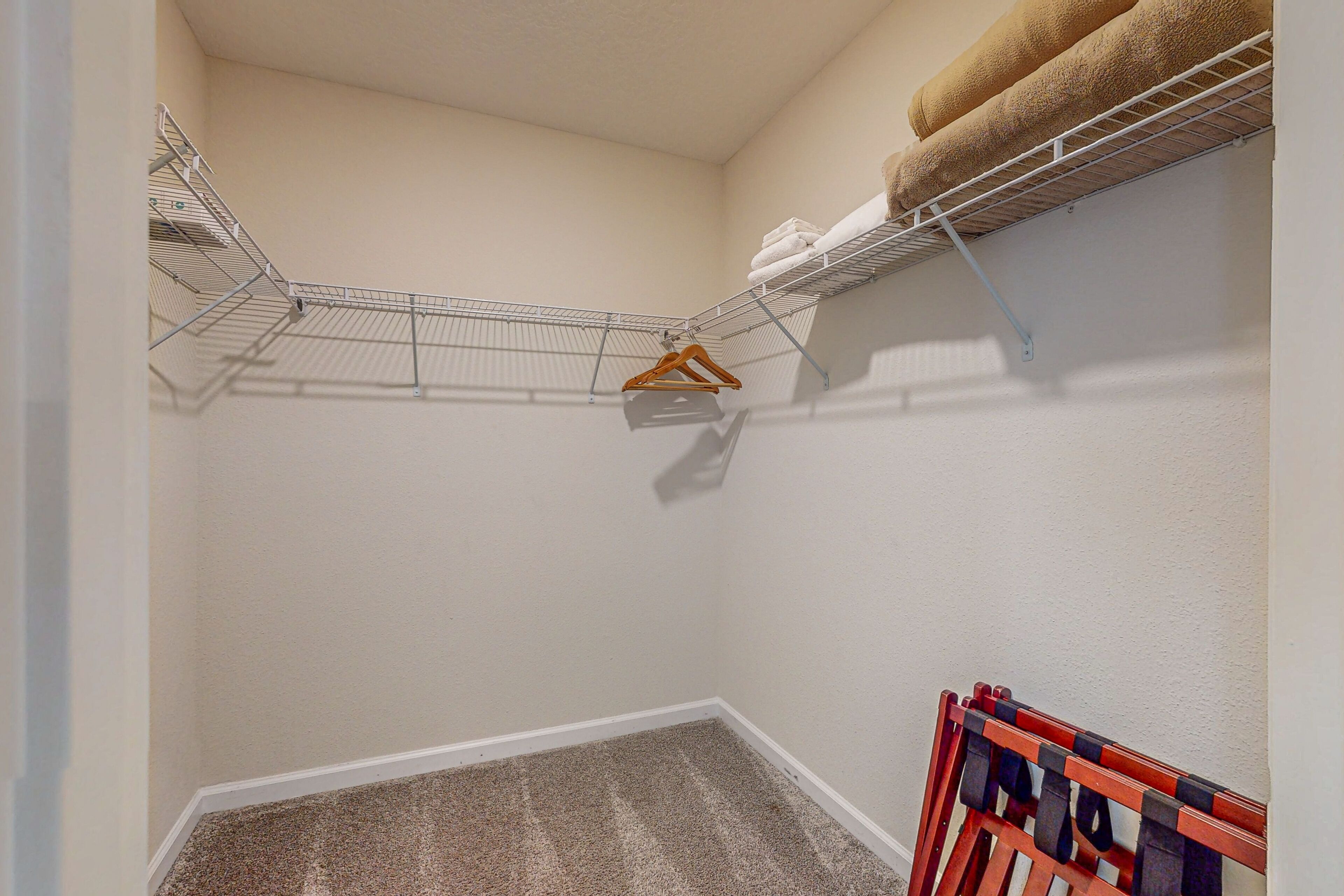 A corner of a room with a wire shelf holding folded towels and a wooden hanger.