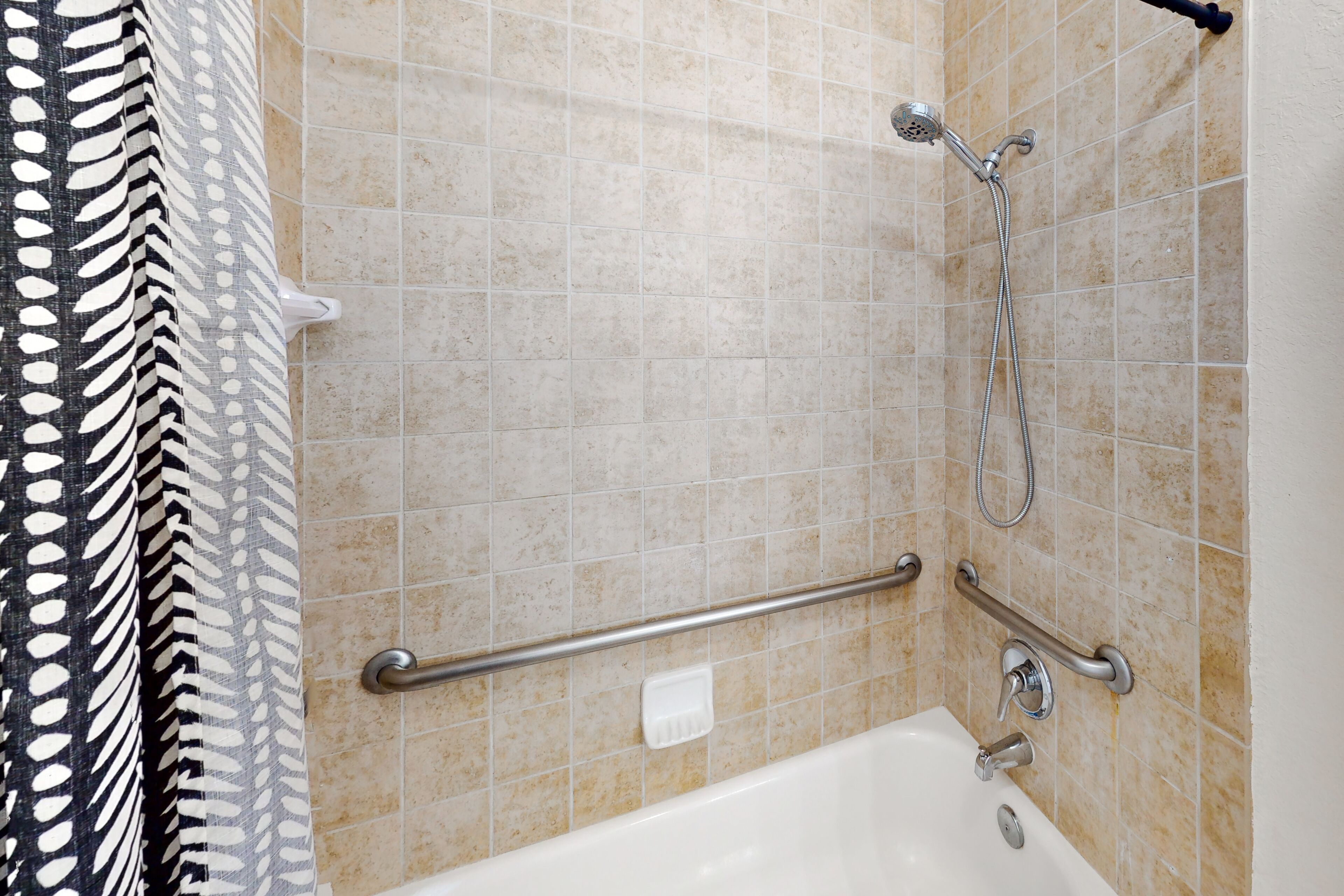 Un baño con bañera, barras de apoyo y cabezal de ducha.