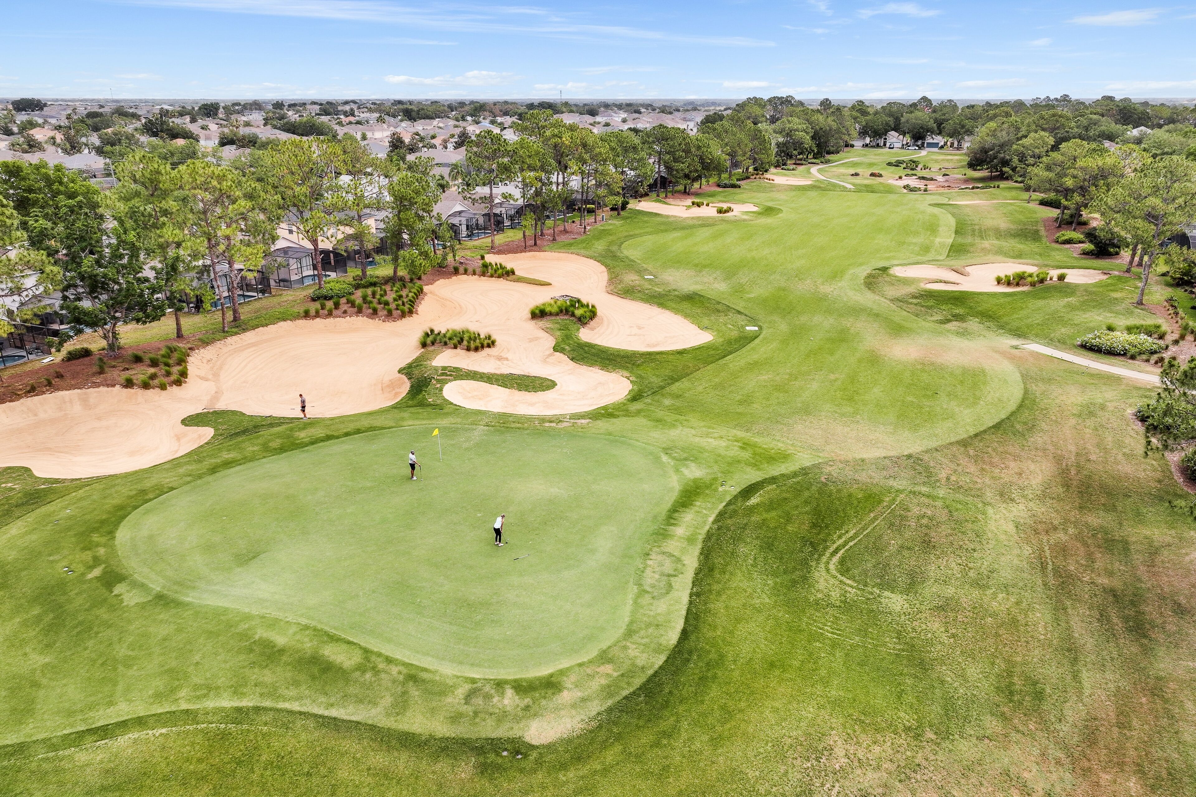 A golf course with sand bunkers, a putting green, and a flag.
