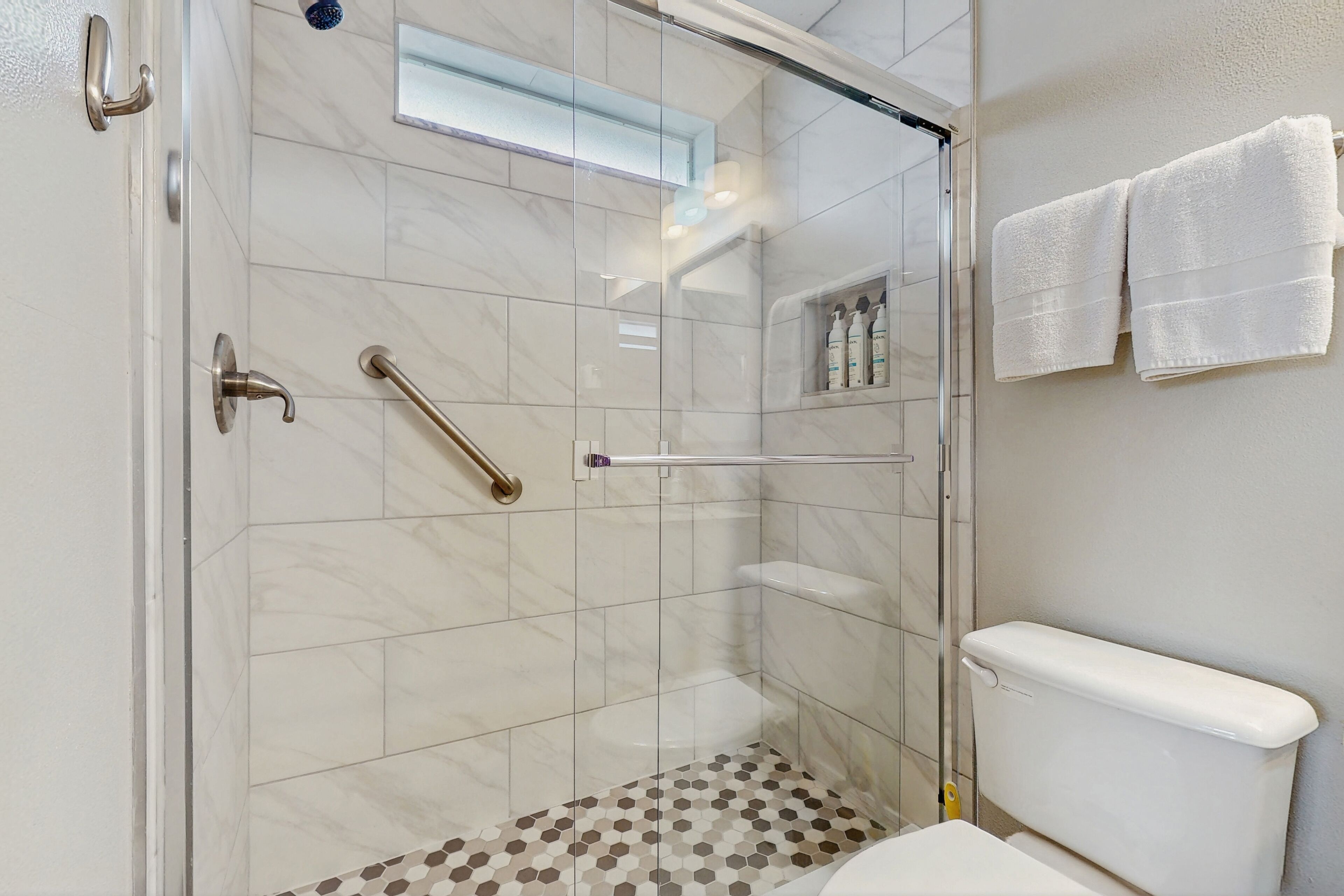 Een moderne badkamer met een douchecabine van glas, een toilet en een plank met toiletartikelen.