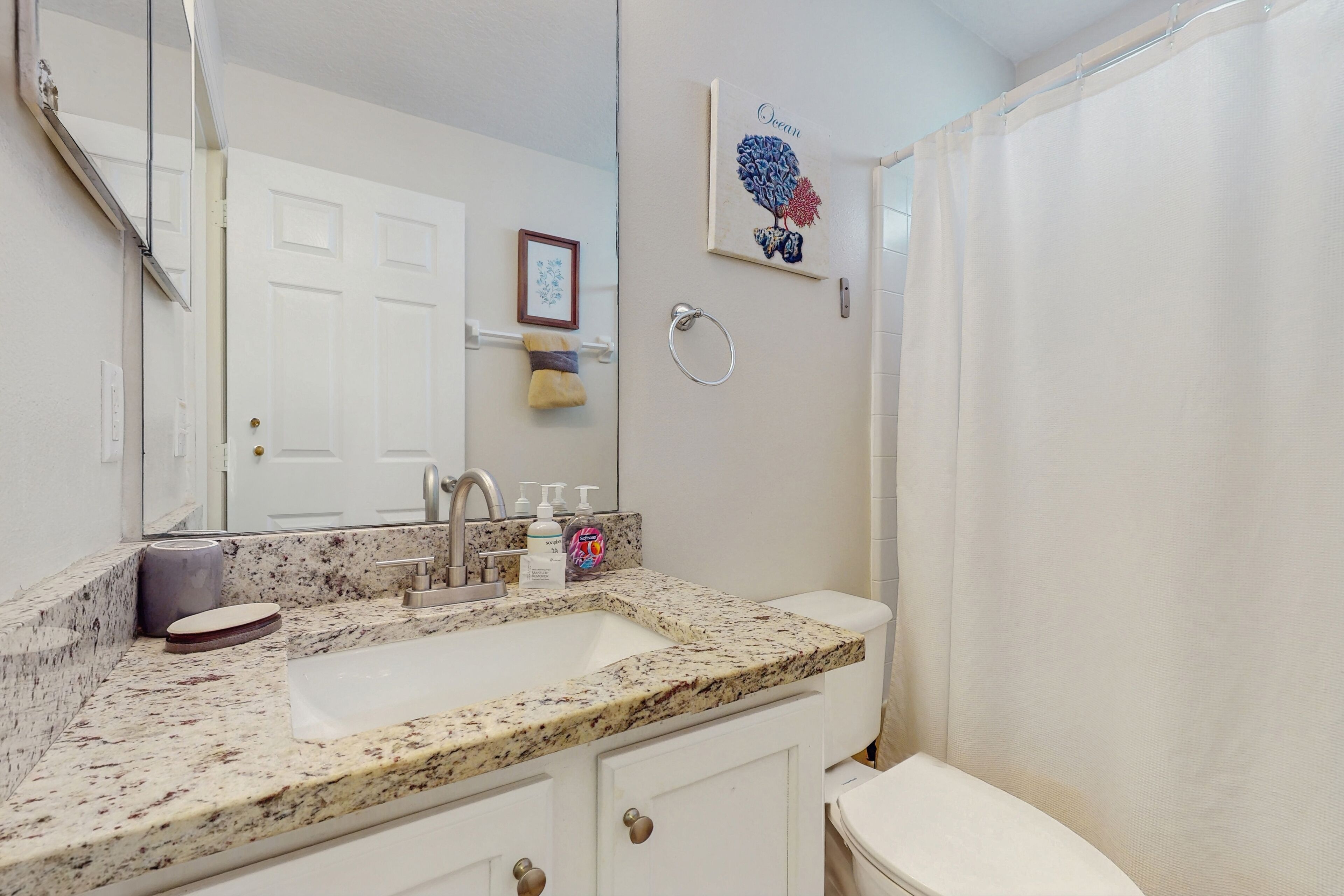 A bathroom with a granite countertop sink, a toilet, a shower curtain, and a mirror.