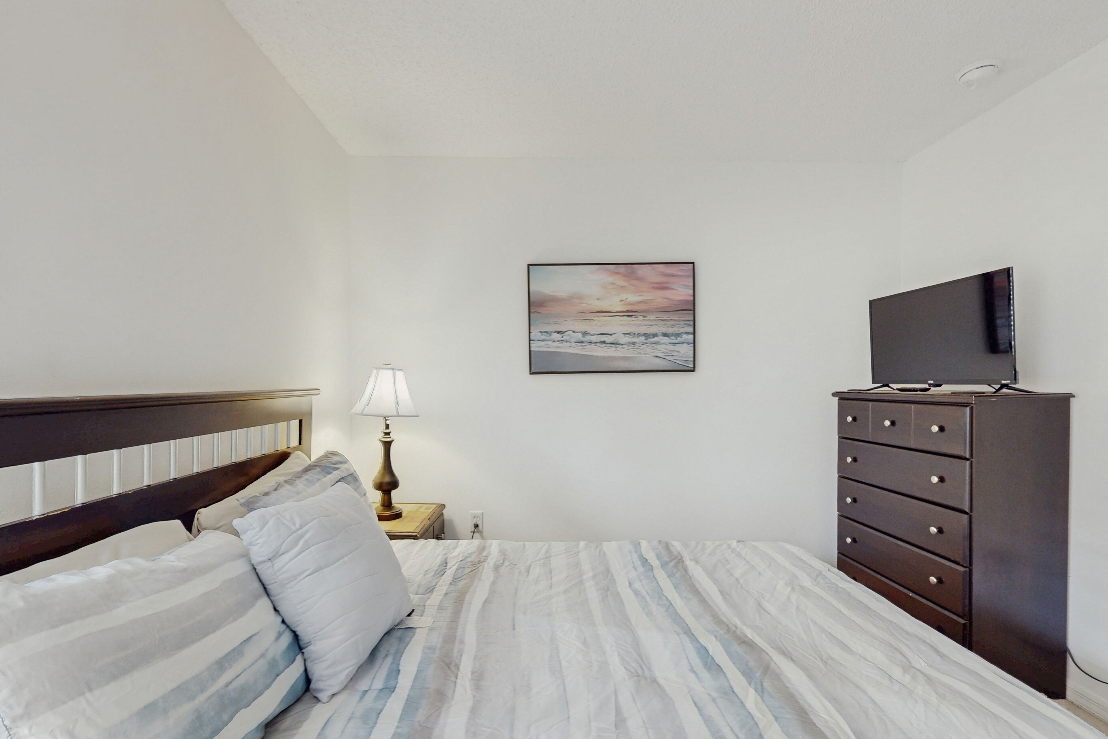 A bedroom with a bed, a dresser, a television, and a painting on the wall.