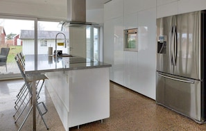 A modern kitchen with white cabinets, a stainless steel refrigerator, and a glass-top island with bar stools. - Beautiful home in Halmstad with WiFi (Halmstad)