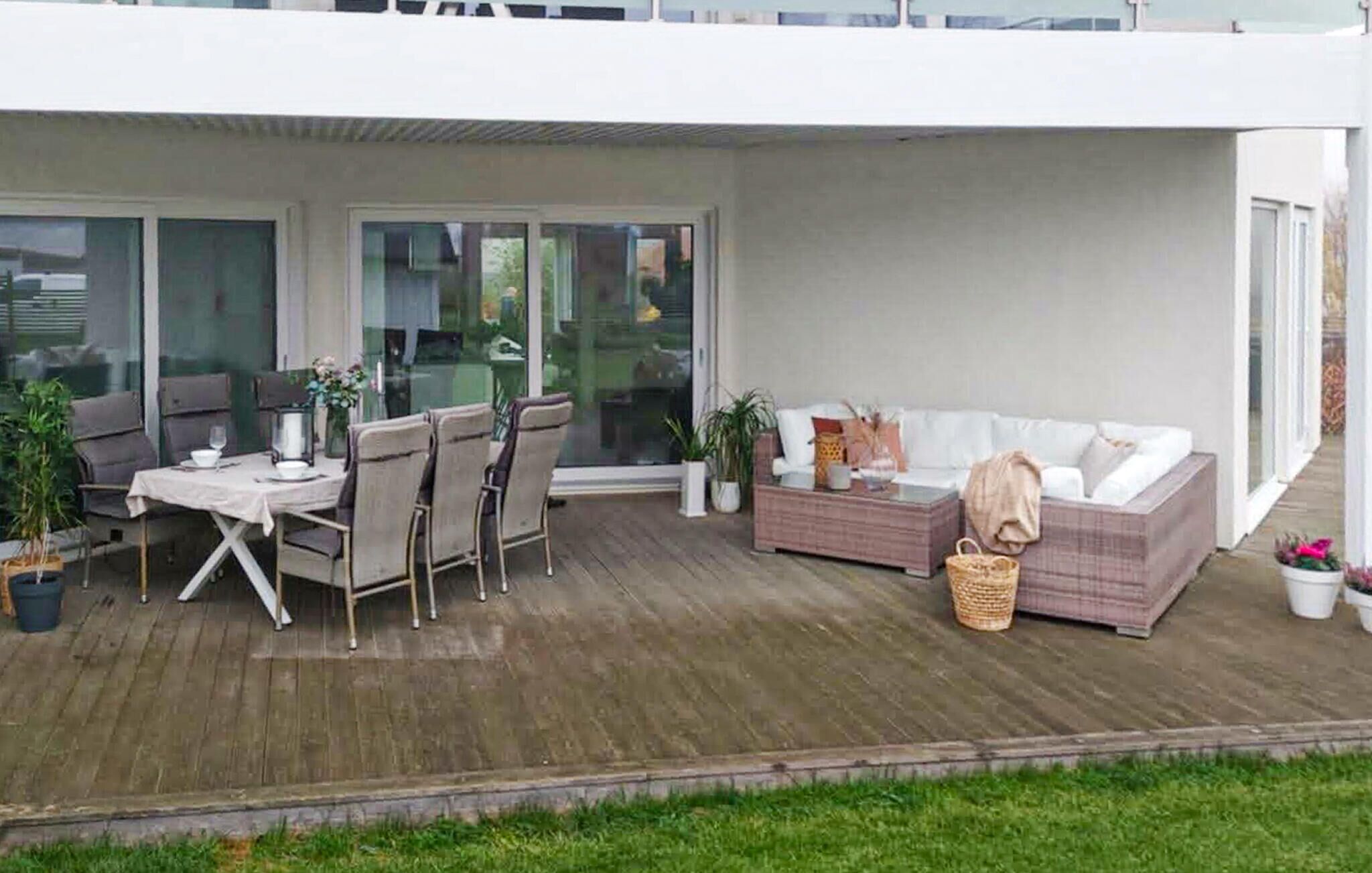 An outdoor patio area with a dining table and chairs, a sofa, and potted plants.