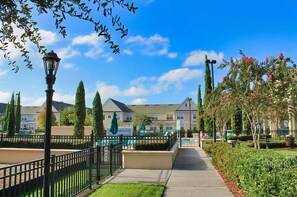 A pathway leading to a building with a pool, surrounded by greenery and a clear sky. - Spacious townhouse with resort style amenities, waterview and fitness center (Kissimmee)