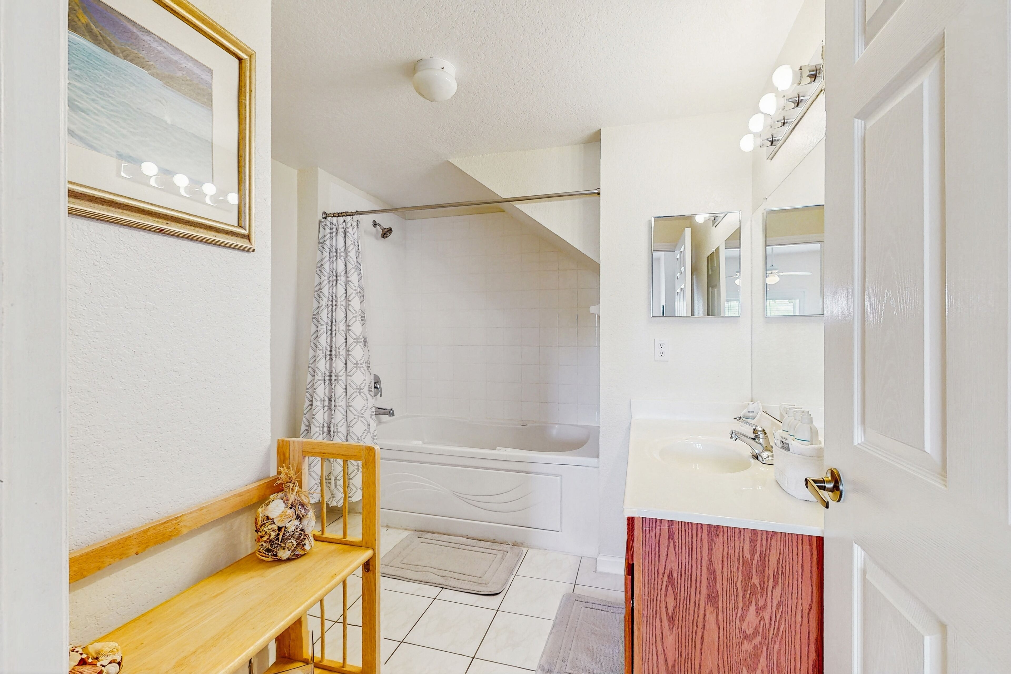 A bathroom with a bathtub, a shower, a sink, a mirror, and a bench.
