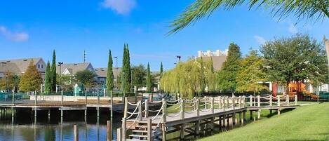 A wooden dock extending over a calm body of water, surrounded by greenery and residential buildings.
