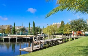 A wooden dock extending over a calm body of water, surrounded by greenery and residential buildings. - Sunset Shores at Venetian Bay | 3BR Water View | Pool (Kissimmee)