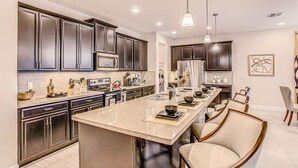 A modern kitchen with dark cabinets, a large island, and bar stools. - Resort home with private pool, patio, foosball & 2 living areas - near Disney (Kissimmee)