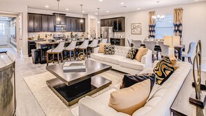 A spacious living room with a large sofa, a coffee table, and a dining area with chairs and a kitchen in the background. - Resort home with private pool, patio, foosball & 2 living areas - near Disney (Kissimmee)
