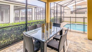 A glass-top table with wicker chairs, a pool, and a view of neighboring houses. - Resort home with private pool, patio, foosball & 2 living areas - near Disney (Kissimmee)