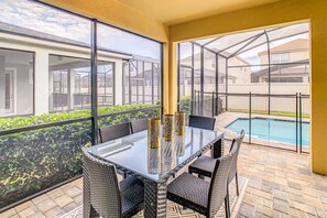 A glass-top table with wicker chairs, a pool, and a view of neighboring houses. - Resort home with private pool, patio, foosball & 2 living areas - near Disney (Kissimmee)