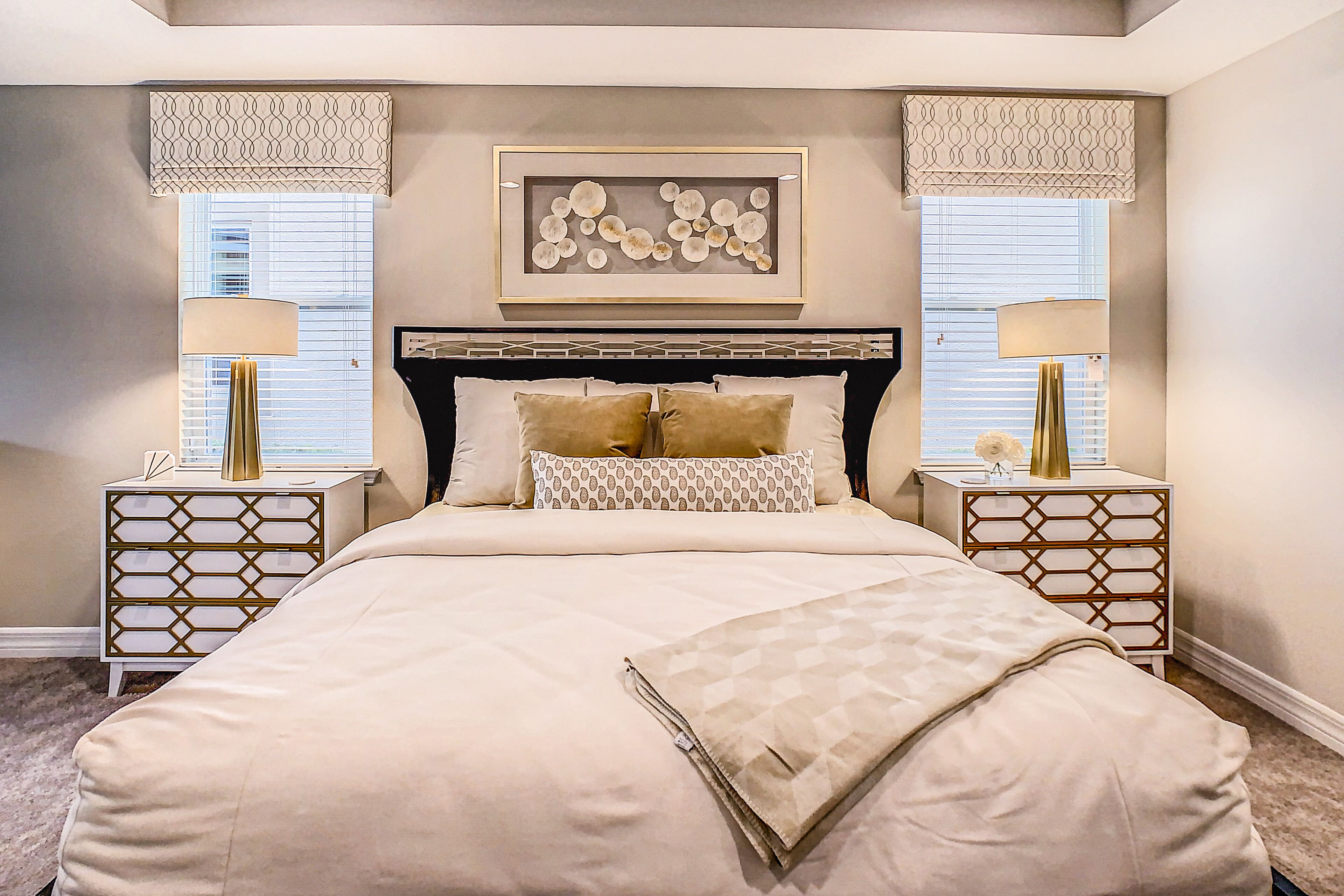 A bedroom with a large bed, two bedside tables with lamps, a decorative headboard, and a framed artwork above the bed.