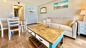 Un salon moderne avec une table basse en bois, des chaises blanches, un canapé beige et une commode blanche.