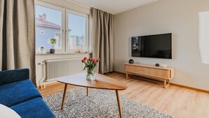 A modern living room with a sofa, a coffee table with a vase of flowers, a TV, and a wooden cabinet. - 1 bedroom nice apartment in Huskvarna (Huskvarna)