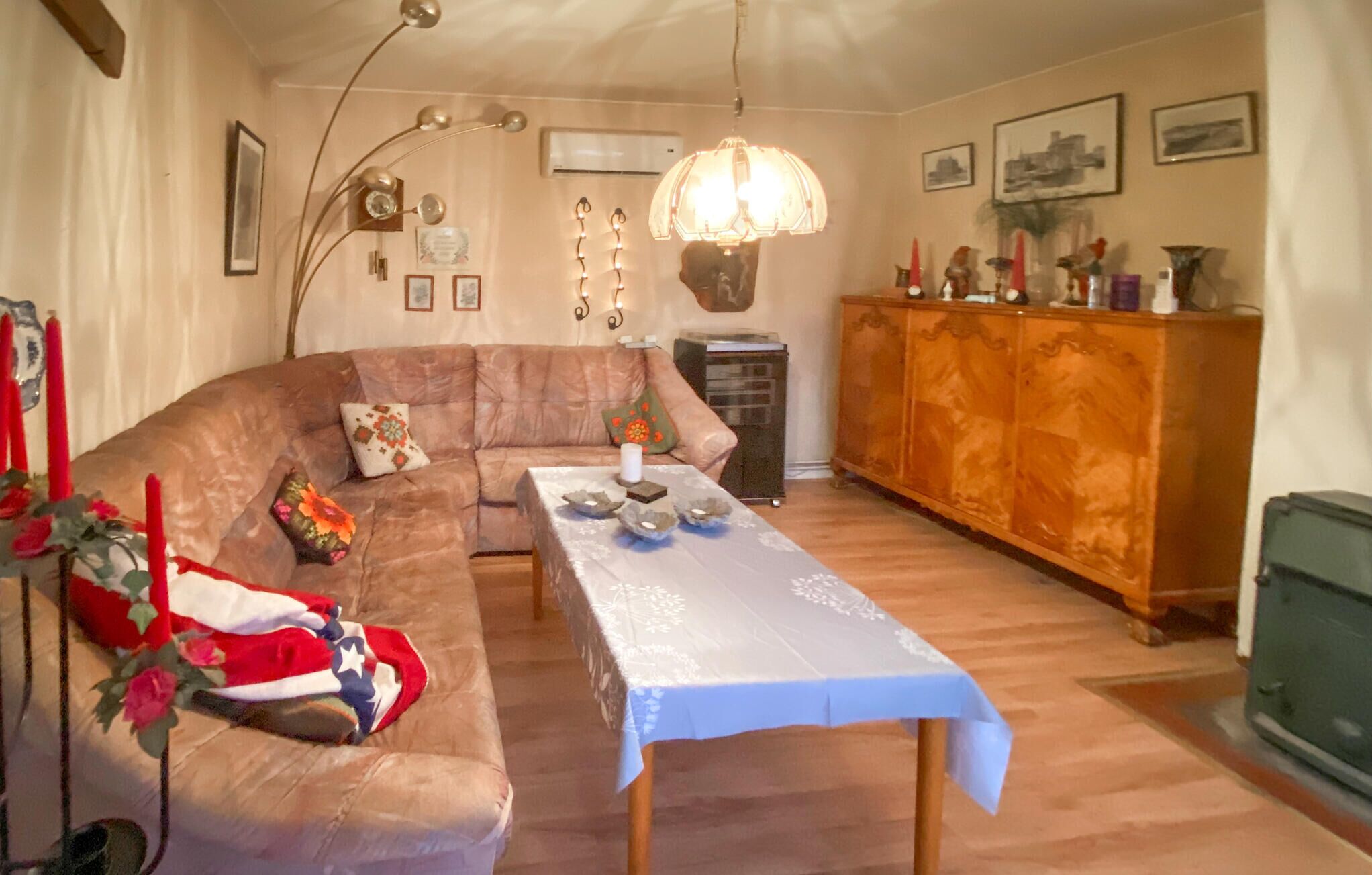A cozy living room with a brown sofa, a dining table with a white tablecloth, and a wooden cabinet.
