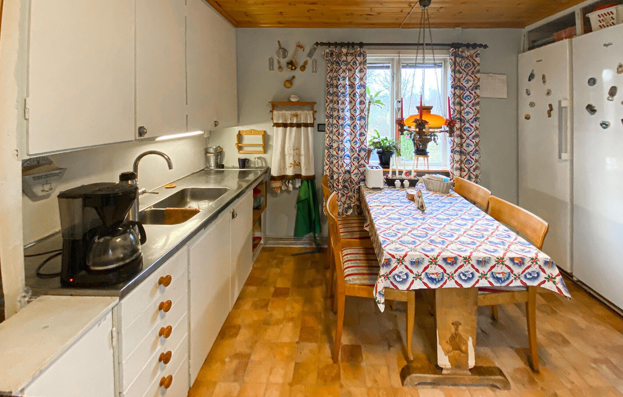 A compact kitchen with a sink, stove, and wooden cabinets. A dining table with a patterned tablecloth is set for two.