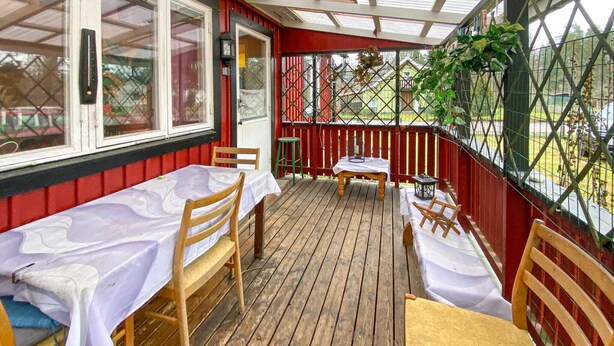 Eine überdachte Terrasse im Freien mit Holztischen und -stühlen, einem kleinen Hocker und einer Laterne.