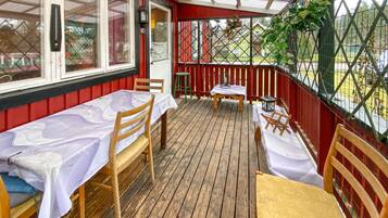 A covered outdoor patio with wooden tables and chairs, a small stool, and a lantern.