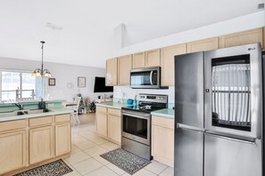 A modern kitchen with stainless steel appliances, wooden cabinets, and a large window. - Snowbird-friendly home near Disney w/private heated pool, lanai, shared tennis (Kissimmee)