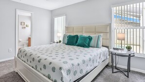 Un dormitorio con cama, ventilador de techo, ventana con rejas y una mesita de noche con lámpara.