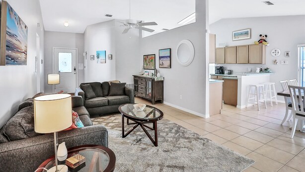 Una sala moderna con un sofá, una mesa de centro y una lámpara. Hay una zona de cocina con armarios y una mesa de comedor.