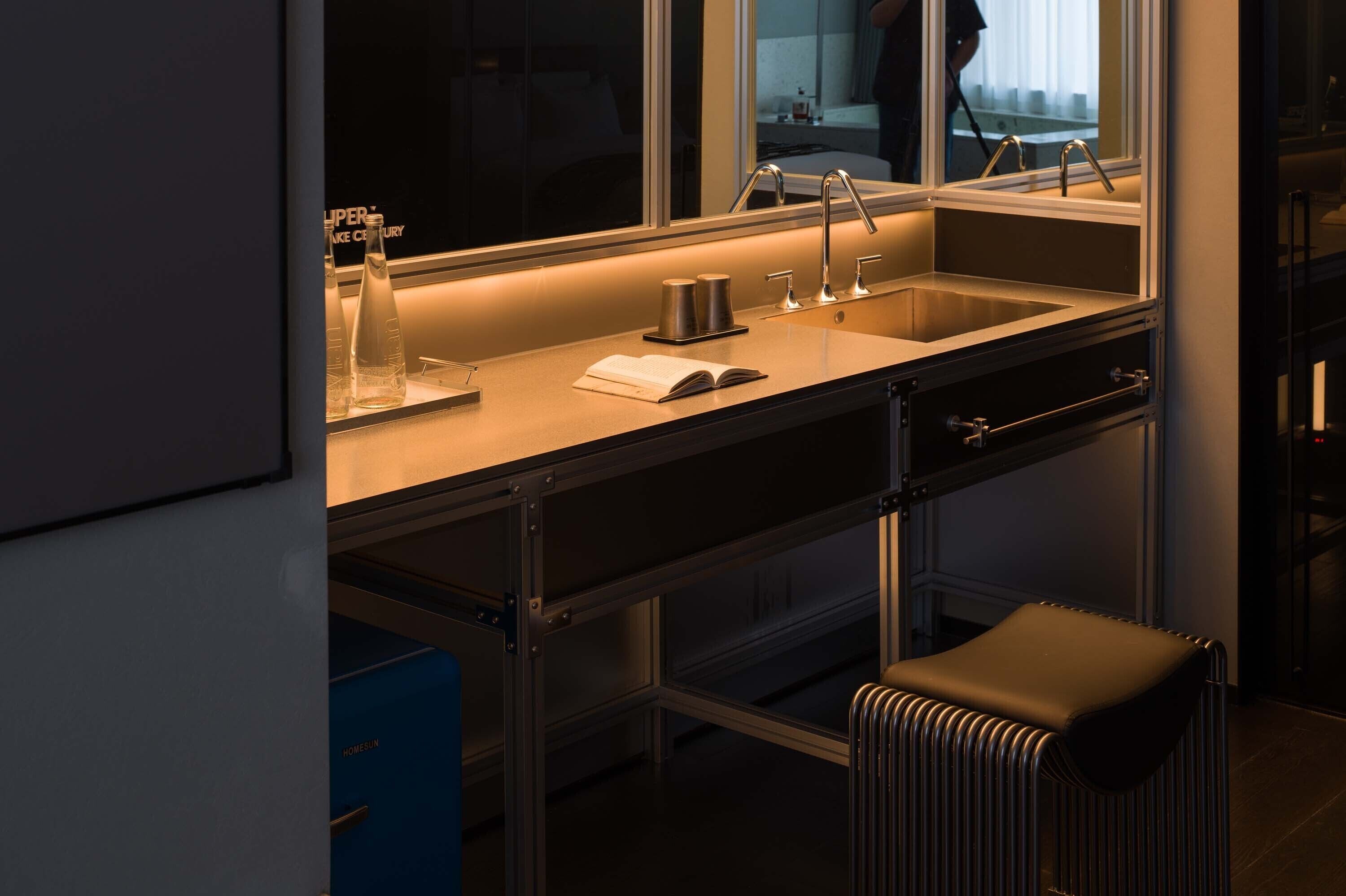A modern kitchen with a stainless steel sink, a window above the sink, and a stool in front of the counter.