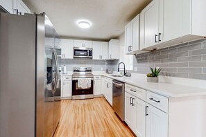 A modern kitchen with white cabinetry, stainless steel appliances, and a tiled backsplash. - Single-story house with private pool, alfresco dining, & lanai - dog-friendly (Kissimmee)