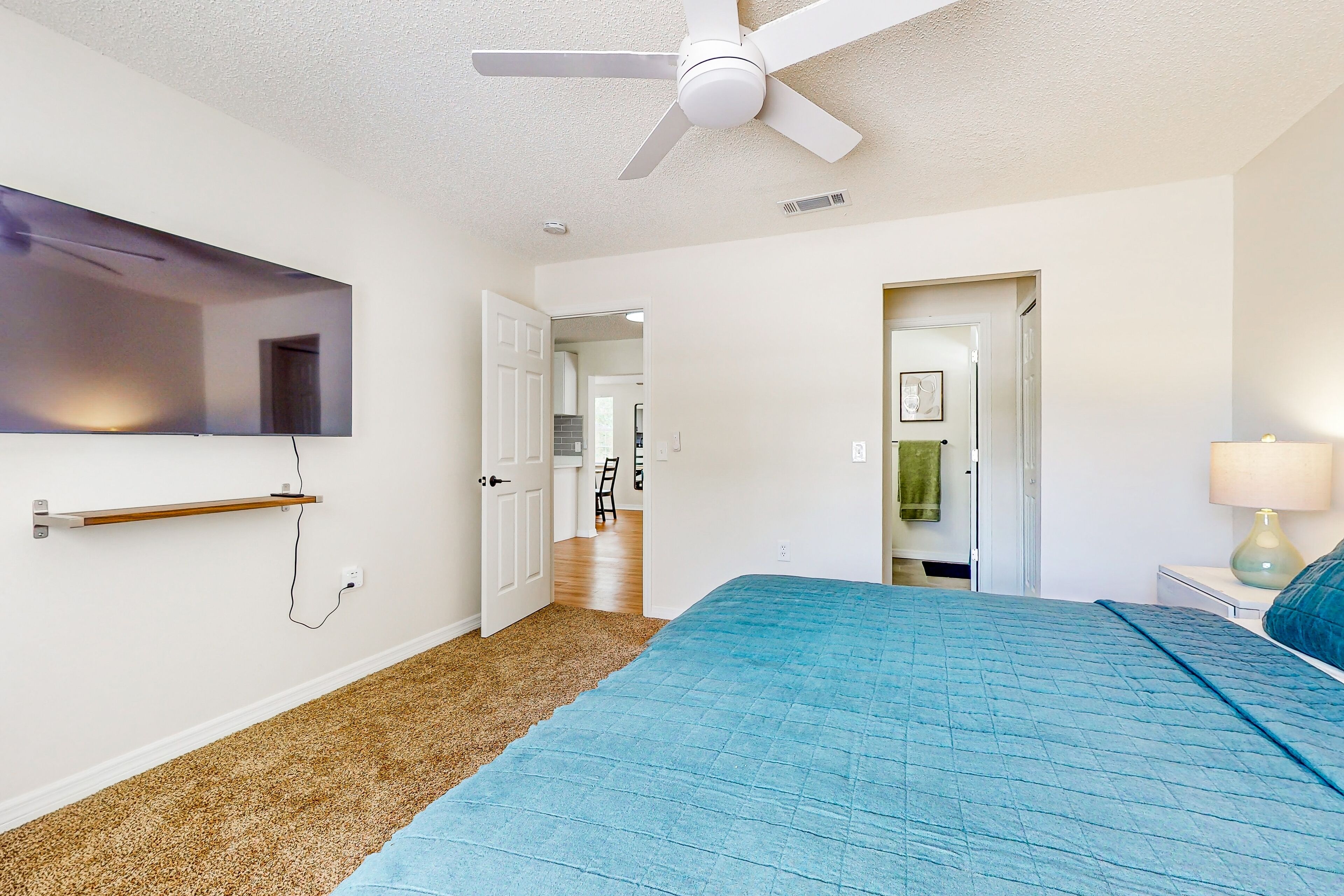 A bedroom with a bed, a ceiling fan, a TV mounted on the wall, and a door leading to a bathroom.