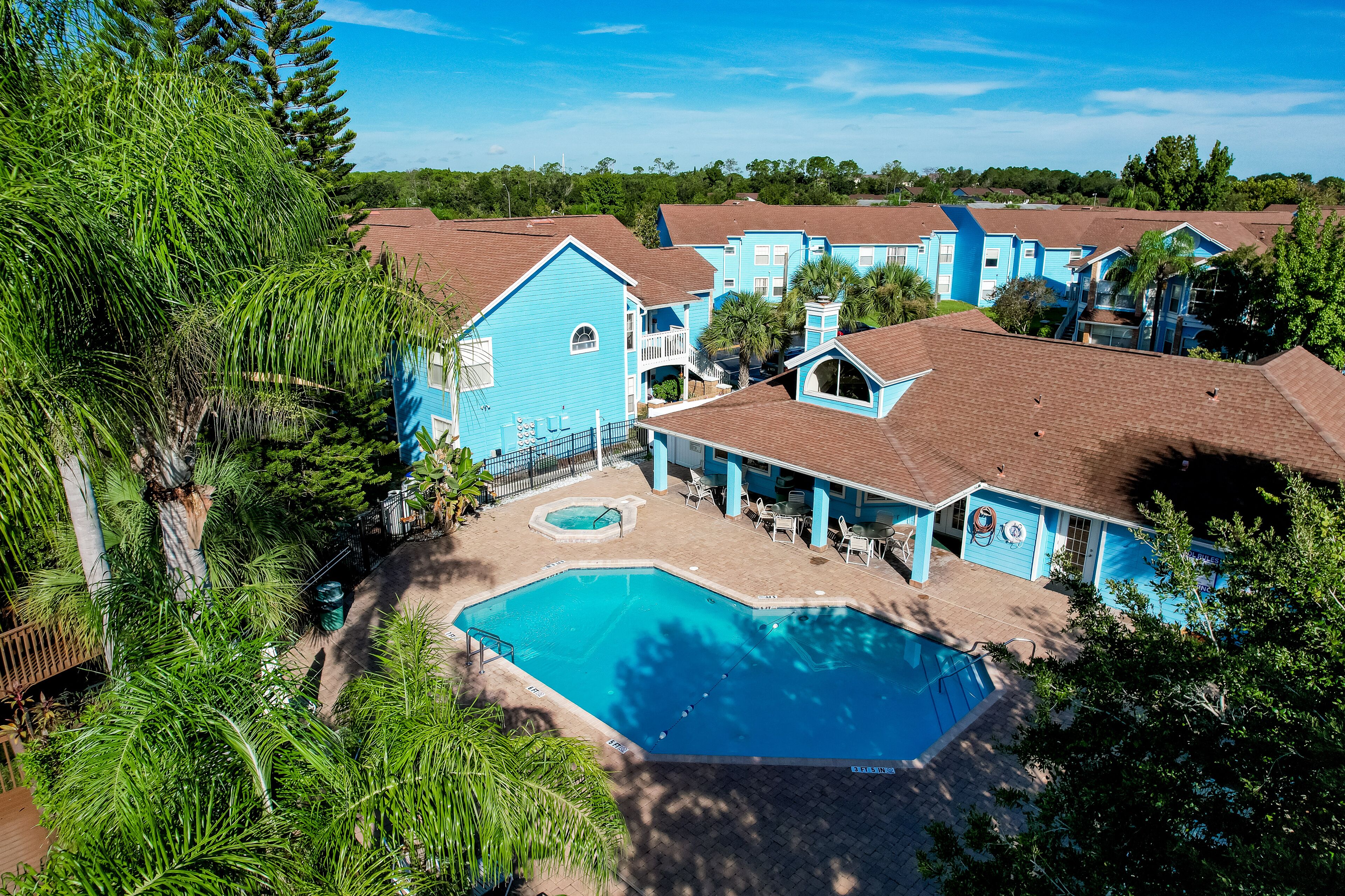 A resort with multiple blue buildings, a central swimming pool, and surrounding greenery.
