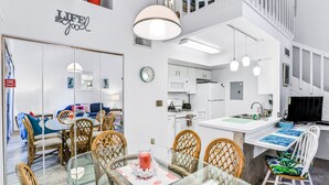 A modern interior with a dining area featuring glass tables and wicker chairs, a kitchen with white cabinets, and a staircase leading to an upper level. - Breezy townhouse with a pool, hot tub, patio, central AC, and washer/dryer (Kissimmee)