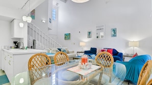 A modern kitchen with white cabinets, a dining area with a glass table, wicker chairs, and a blue sofa. - Breezy townhouse with a pool, hot tub, patio, central AC, and washer/dryer (Kissimmee)