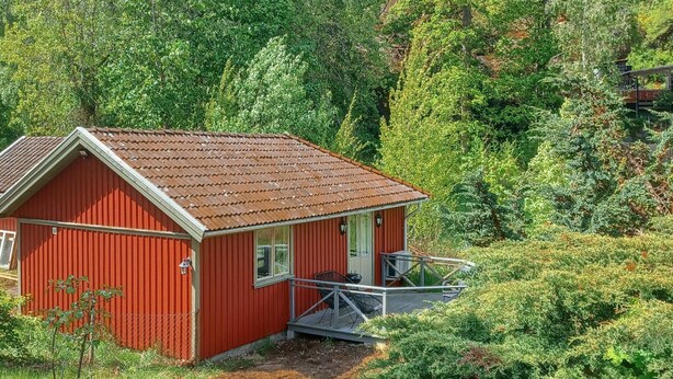Een rode houten chalet met een veranda, omringd door dicht bos.