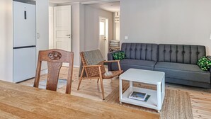 Een woonkamer met een grijze bank, een houten stoel, een witte salontafel en een witte kast.