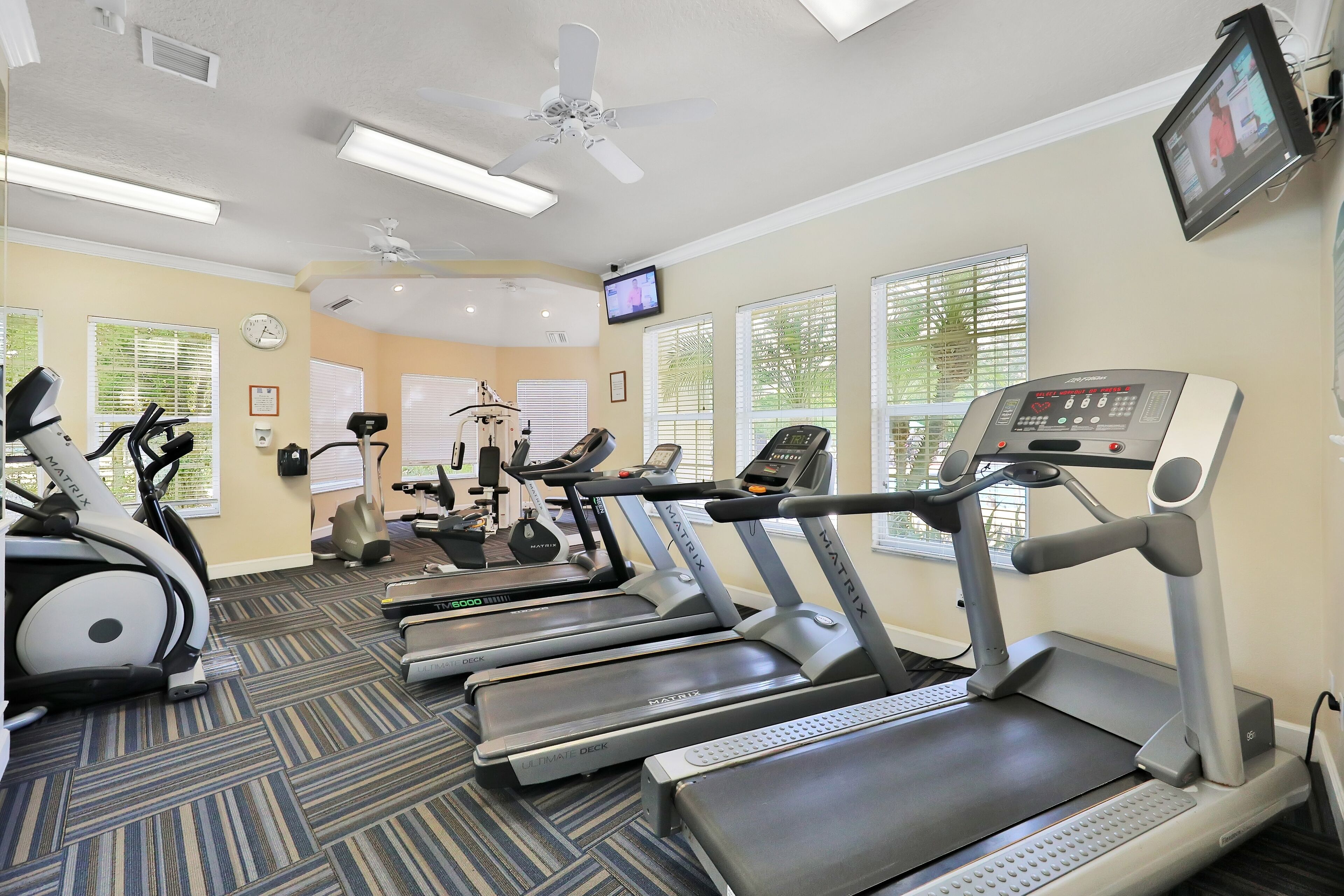 A fitness center with treadmills, elliptical machines, and a television screen.