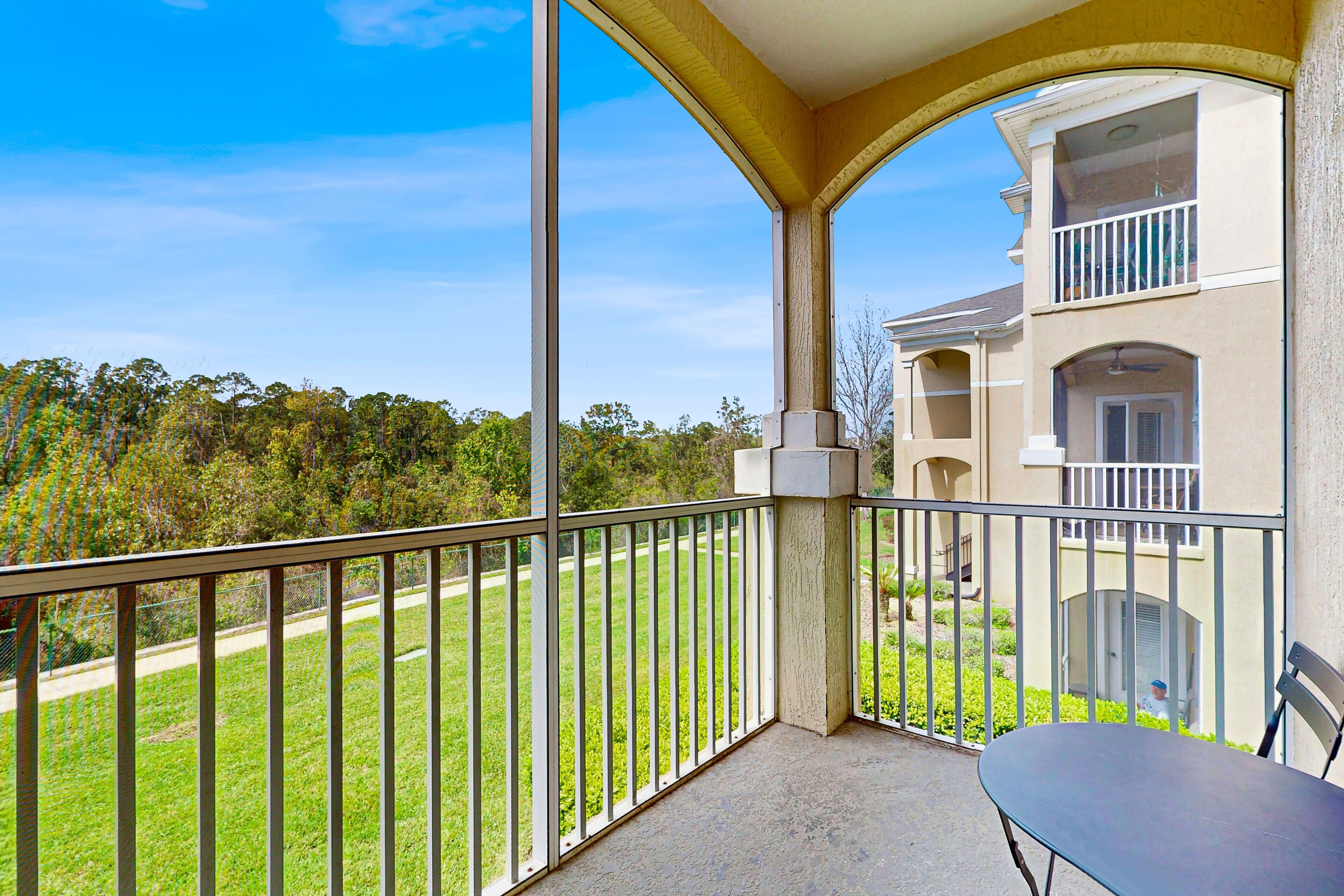 A balcony with a view of a green lawn and a building in the background.