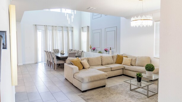 Un salon spacieux avec un grand canapé d’angle, une table basse en verre et un coin repas comprenant une table et des chaises.