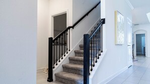 Un escalier avec une rampe noire et des marches recouvertes d’un tapis beige, menant à une porte.