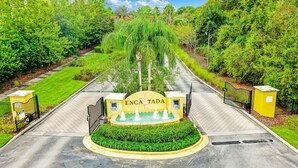 A gated entrance with a fountain, surrounded by lush greenery and a clear sky. - Two-story, dog-friendly gem near theme parks with pool, central AC & on-site gym (Kissimmee)