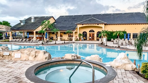 Un espace piscine avec des chaises longues, un jacuzzi et un bâtiment doté d’un espace extérieur aménagé pour s’asseoir.
