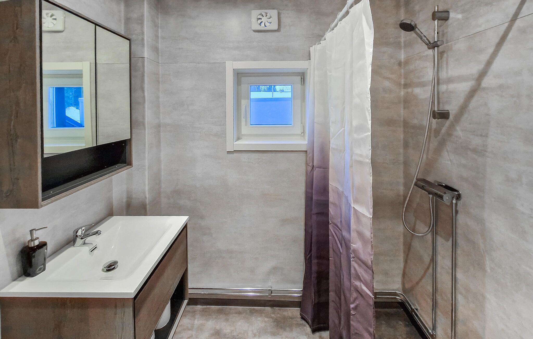 A bathroom with a white sink, a mirror, a shower, and a window.
