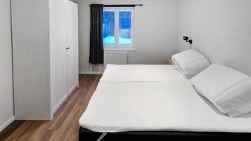 A bedroom with a bed, a window with curtains, a wardrobe, and a bedside table with a lamp.