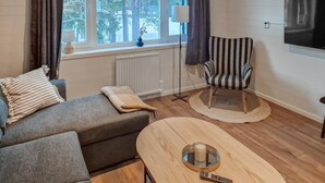 A cozy living room with a sofa, a striped armchair, a round coffee table with a candle, and a view of trees through the window. - Pet friendly apartment in Kåbdalis with WiFi (Kåbdalis)