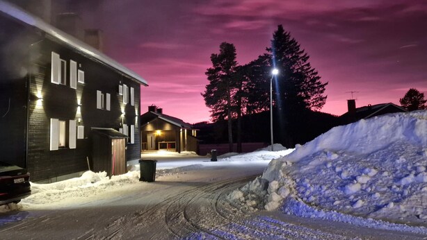 A snow-covered street with a house on the left and a snow pile on the right.