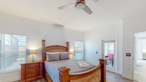 Ein Schlafzimmer mit einem hölzernen Bett, Nachttischen, einem Deckenventilator und großen Fenstern.
