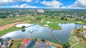 Een golfbaan met een vijver, een brug en een groot gebouw op de achtergrond.