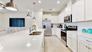 Une cuisine moderne avec des meubles blancs, des appareils en acier inoxydable et des luminaires suspendus.